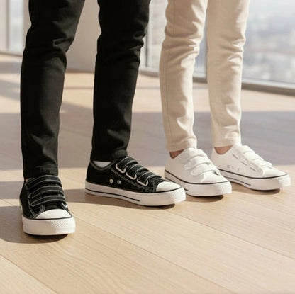 Two pairs of feet wearing black and white eluxeri canvas on a wooden floor.