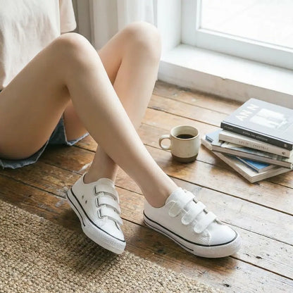 Person wearing white Eluxeri Canvas on a wooden floor with a cup of coffee and books in the background.