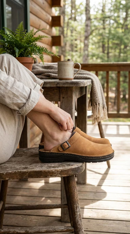 Person wearing tan shoes sitting on a wooden stool with a cup and plant in the background.