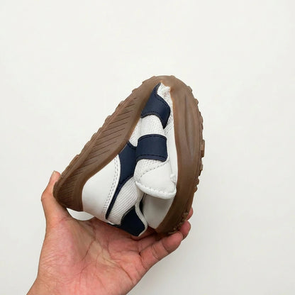 Hand folding a barefoot shoe with brown sole and white and navy upper against a light background