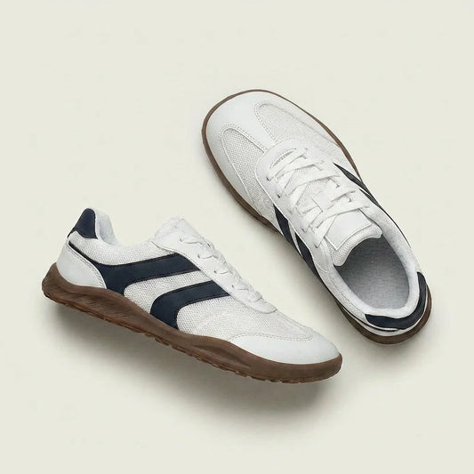 White sneakers with navy accents and brown soles on a light beige background
